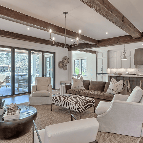 Exposed wooden beams add rustic charm to this modern living room with large windows and cozy seating.
